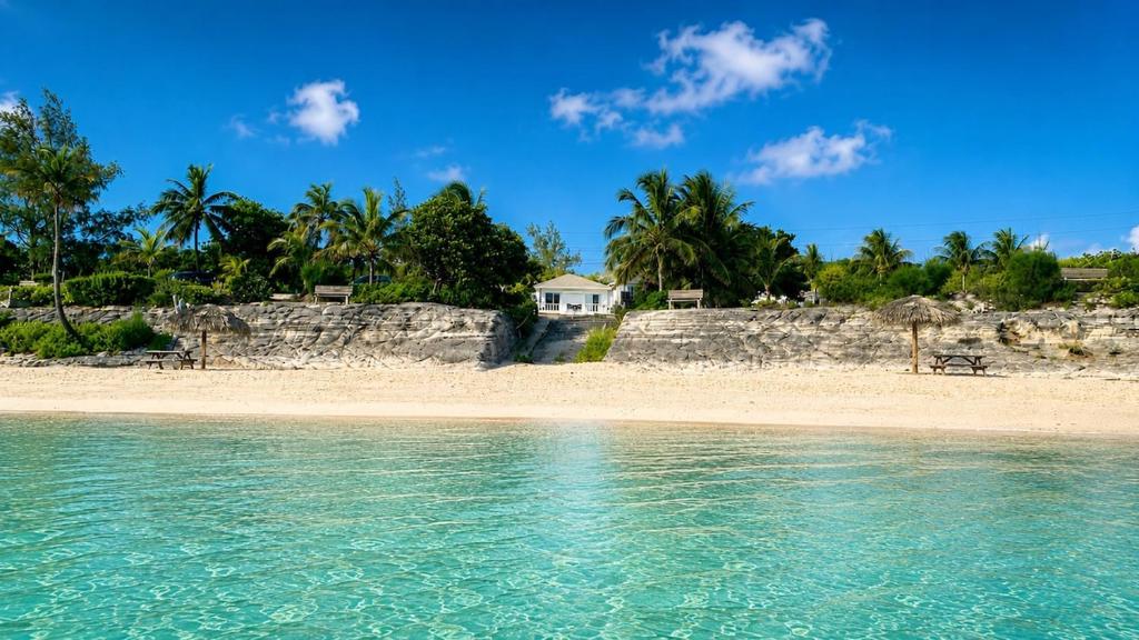 a beach with a white house in the distance at The Anchorage at Rainbow Bay, Eleuthera in Hatchet Bay Limited Settlement