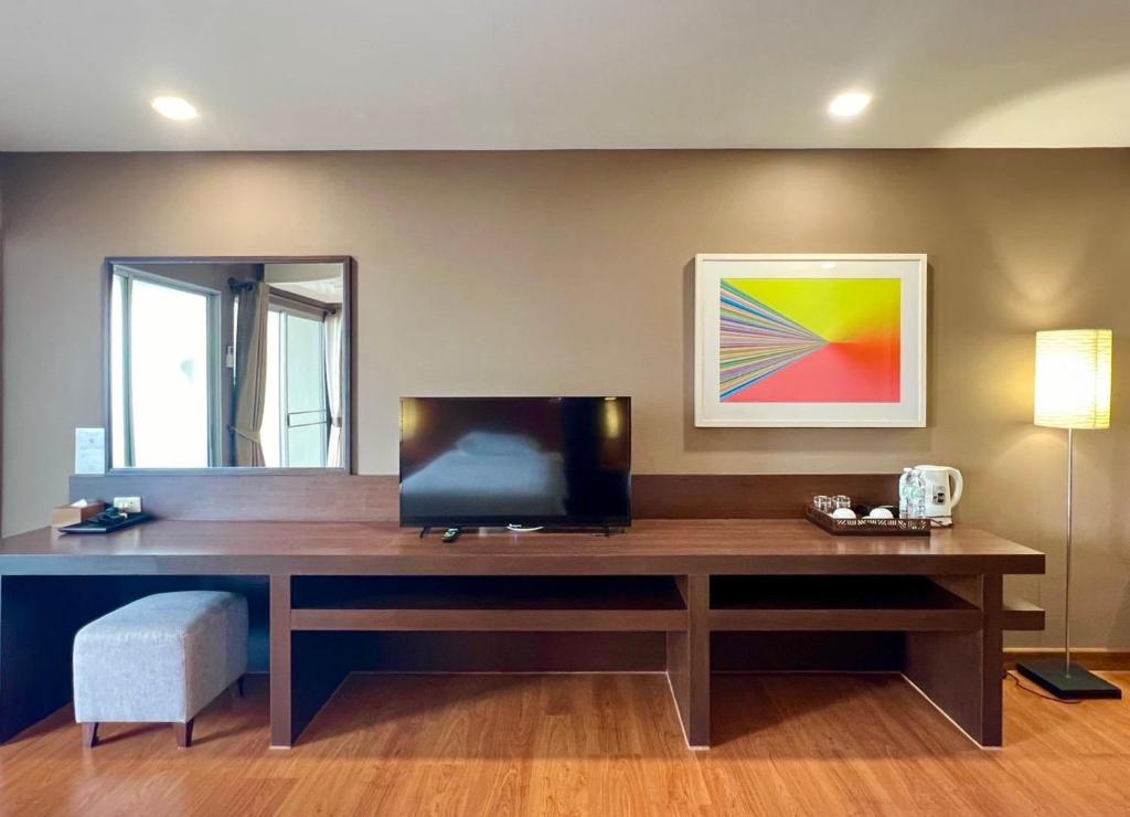 A long wooden console with a television, mirror, tea setup and small seat.