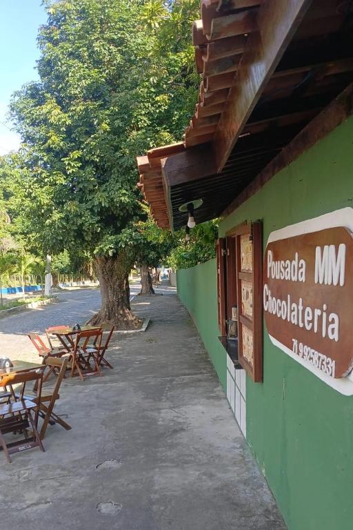 a building with tables and chairs next to a tree at Pousada e Chocolateria Muito Mais in Itaparica