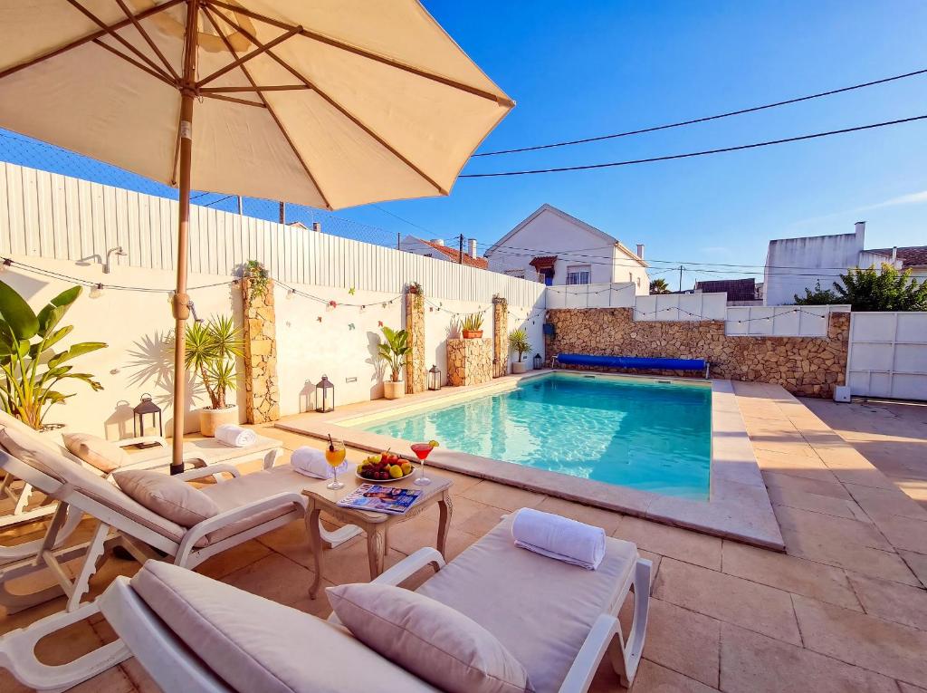 a pool with chairs and an umbrella on a patio at Private Pool House Minutes from the Beach in Charneca