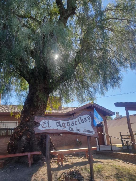 a sign sitting under a tree next to a bench at El Aguaribay de los Nonos in Mina Clavero