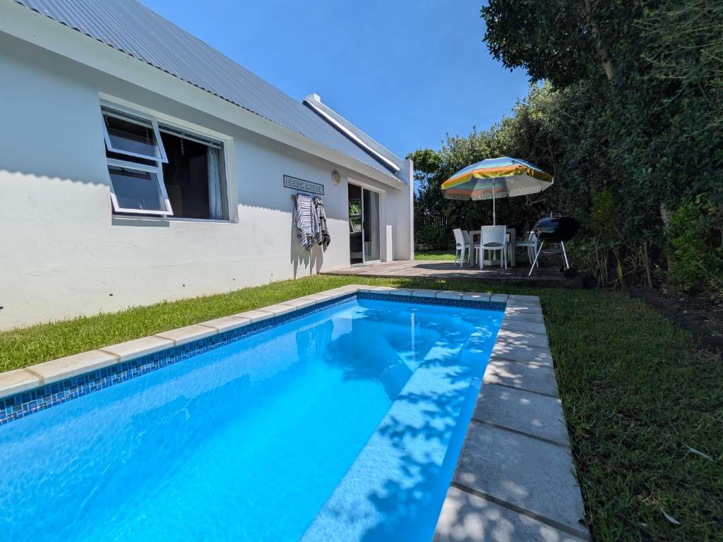 a swimming pool in front of a house with an umbrella at Cape St Francis Beach Cottage in Cape St Francis