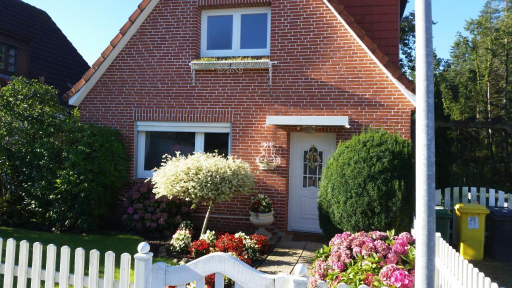 ein rotes Backsteinhaus mit einem weißen Zaun und Blumen in der Unterkunft Ferienhaus am Hasselberg Husum in Husum