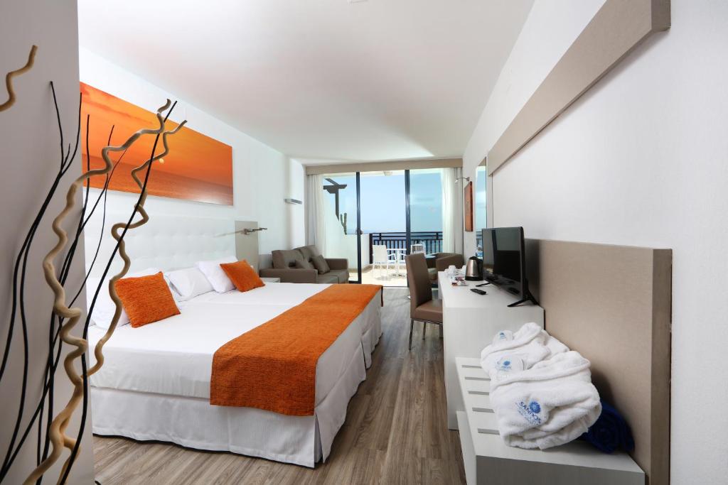 a bedroom with a bed and a desk with a television at Sandos Papagayo in Playa Blanca