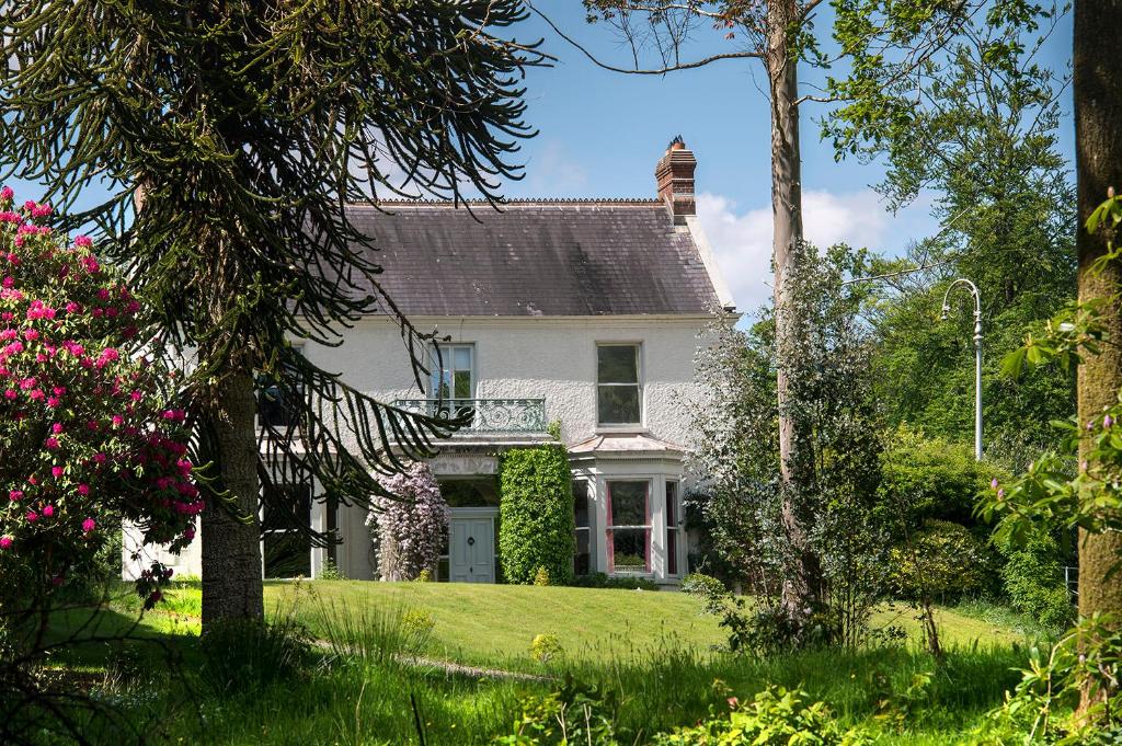 una casa bianca con un cortile con alberi e fiori di Ballyteige Lodge a Ballyteige Bridge