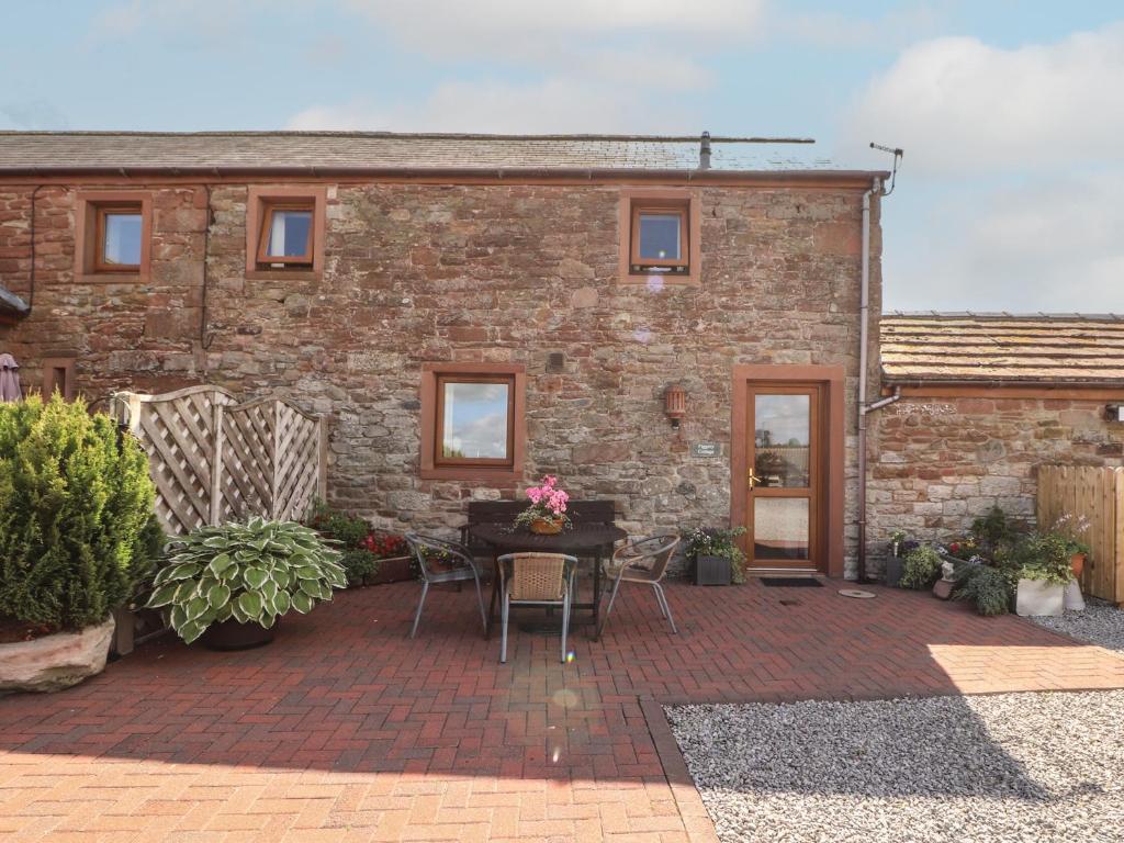a brick house with a patio with a table and chairs at Piggery Cottage in Wigton