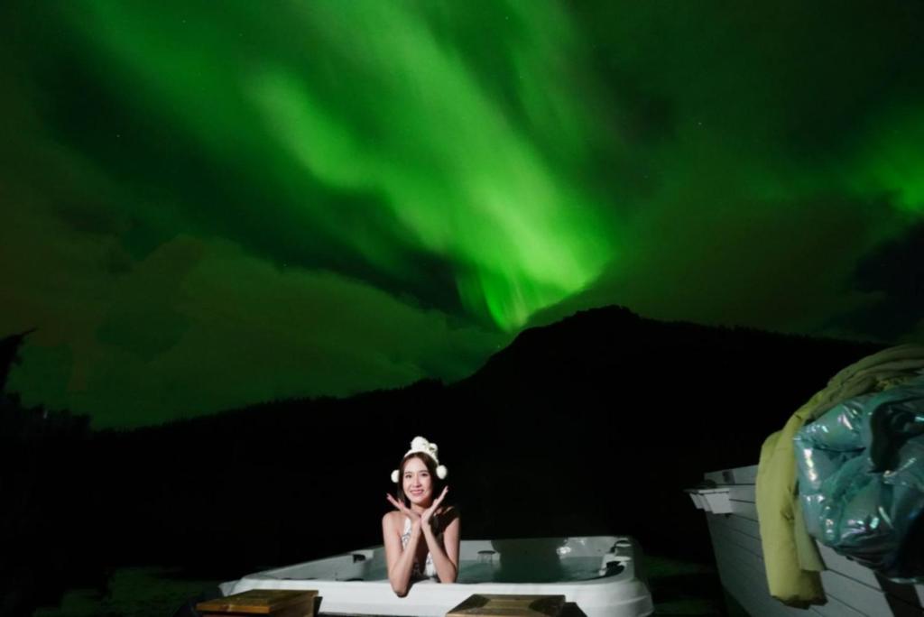 a woman sitting in a bathtub under the northern lights at Banpim apartment with Jacusszi in Gravdal
