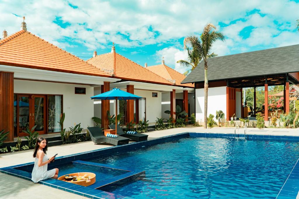 a woman sitting next to a swimming pool in a villa at The Siantar Luxury Villa And Spa in Nusa Penida