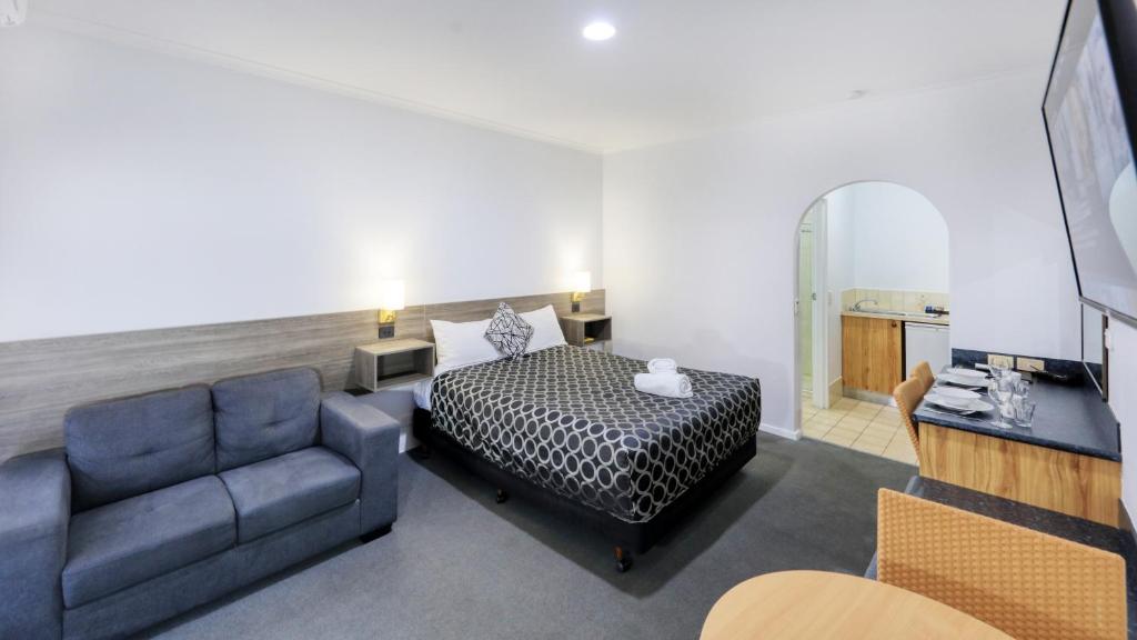 a bedroom with a bed and a couch and a mirror at The Cottage Motor Inn Albury CBD in Albury