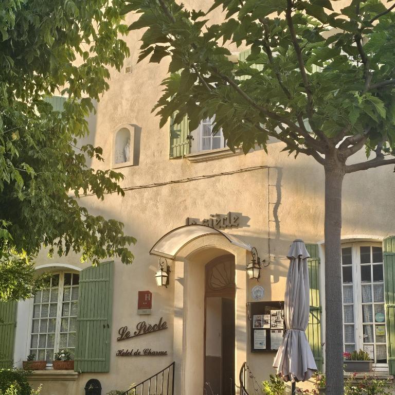 a building with an umbrella next to a tree at Hôtel Le Siècle in Mazan
