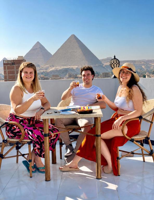 three people sitting at a table in front of the pyramids at malak pyrameds rofe top in Cairo