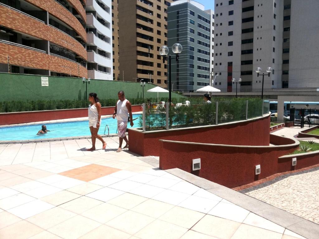 dos personas caminando por una piscina en una ciudad en AP Top Condominio Porto de Iracema, en Fortaleza