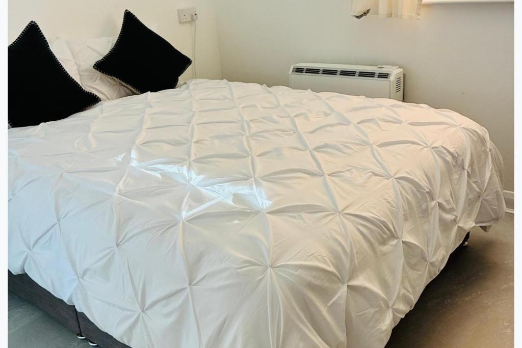 a large white bed in a room with black pillows at Cozy Grays Apartment in Grays Thurrock