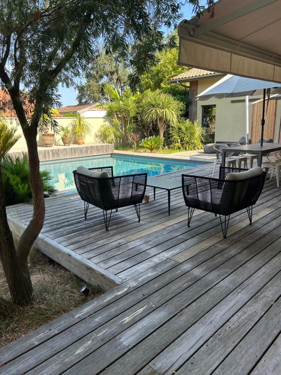 a wooden deck with chairs and a table next to a pool at Les mimosas in Tosse