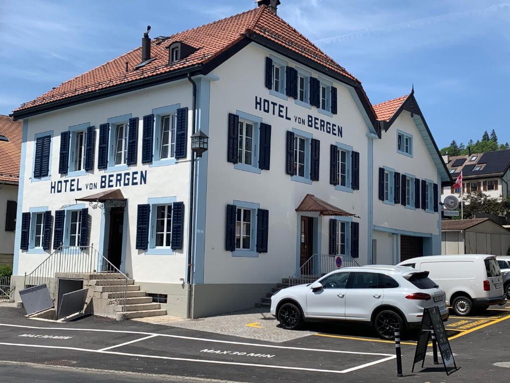 a white building with a car parked in a parking lot at Hôtel Von Bergen in La Sagne