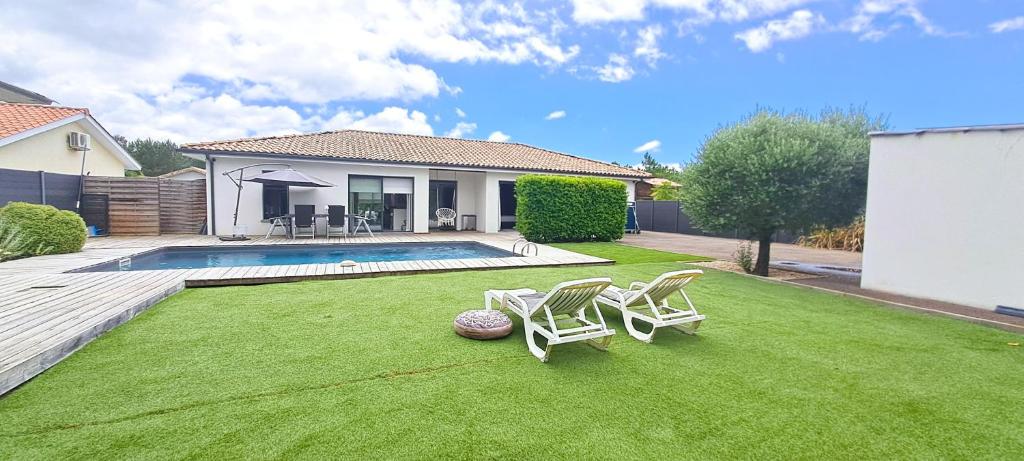a yard with two chairs and a swimming pool at Jolie villa avec piscine chauffée proche du lac in Sanguinet