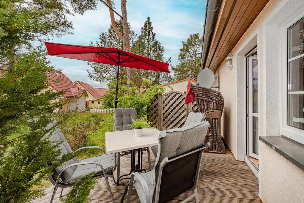 a patio with a table and chairs and a red umbrella at Waldsiedlung Waldhaus App 4.1 in Korswandt
