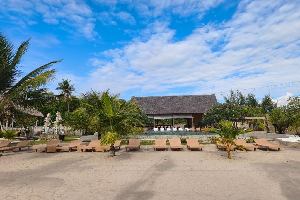 a beach with chairs and a building and palm trees at Maruti Beach Villas in Nusa Penida