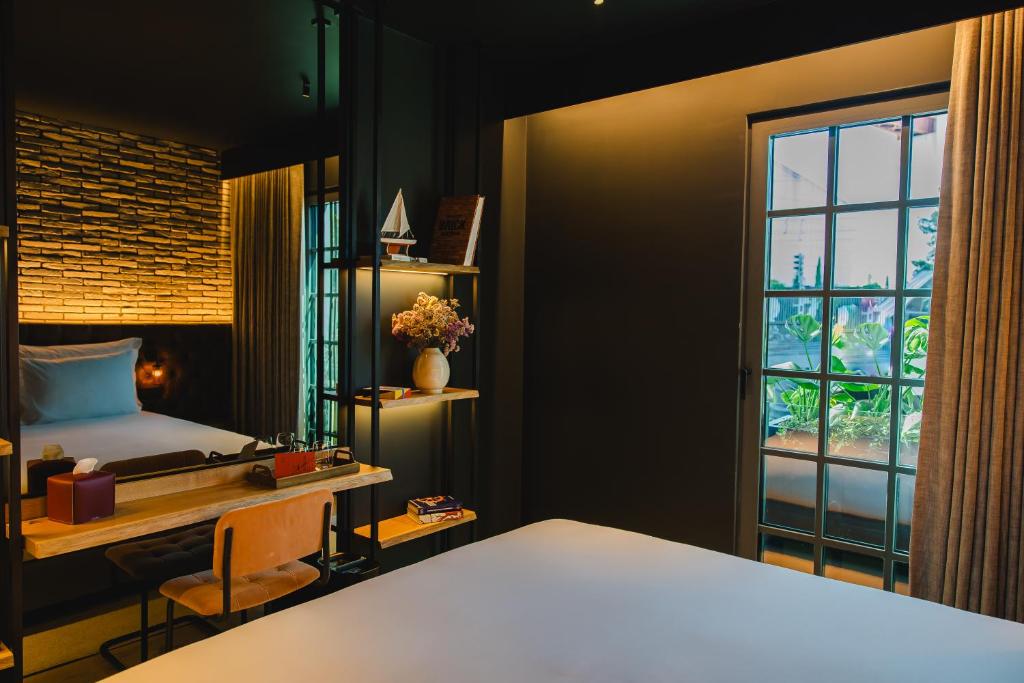 A darkly styled bedroom combines a large bed, desk, shelving, and tall windows.