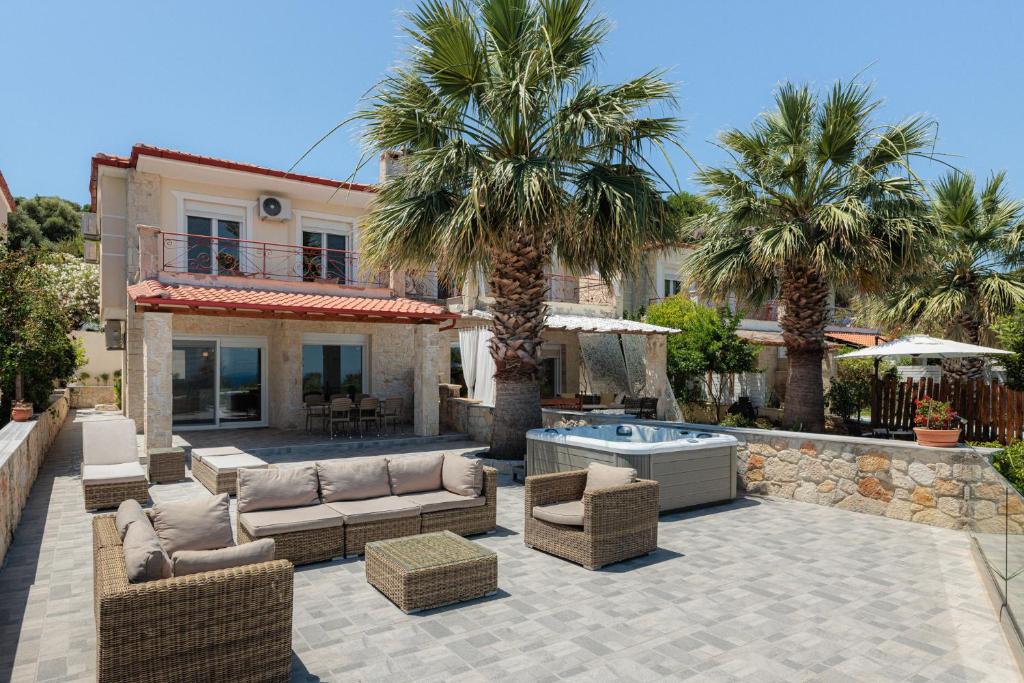 a patio with couches and palm trees in front of a house at Azura Villa #Skgbnb in Mesochórion