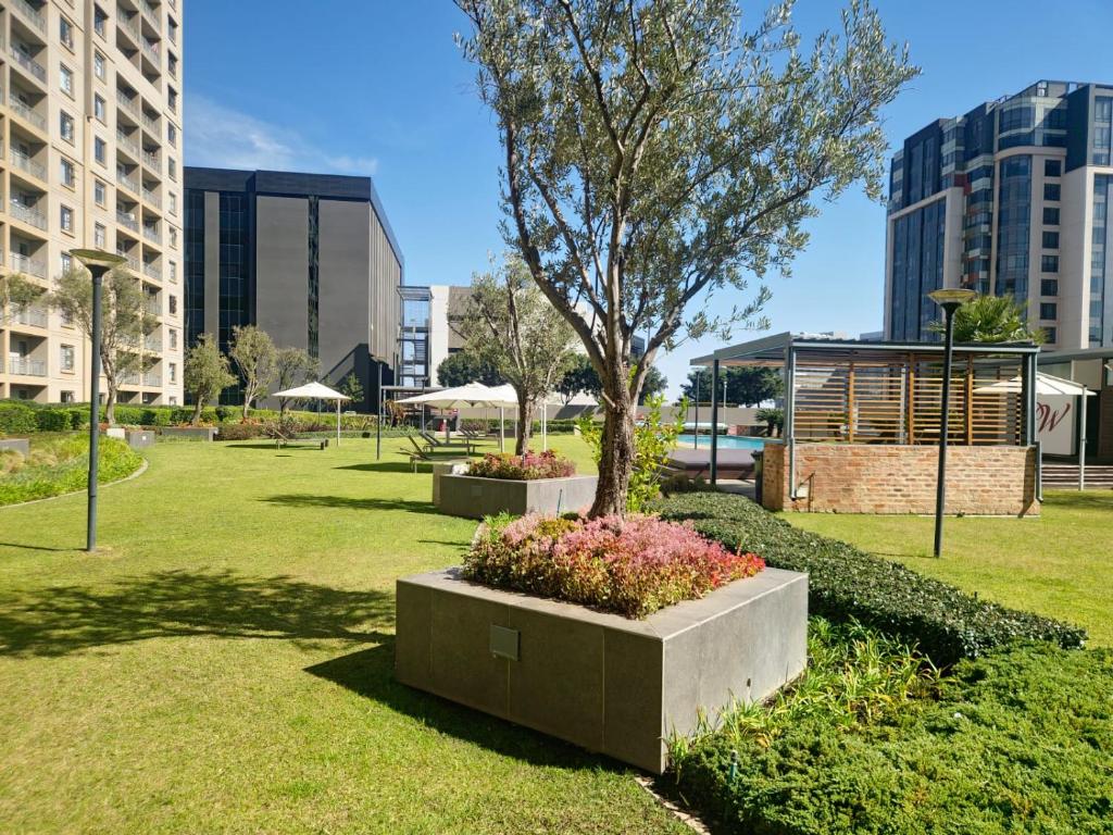 a park with a tree and flowers and buildings at Prestige Apartments Sandton at Westpoint in Johannesburg