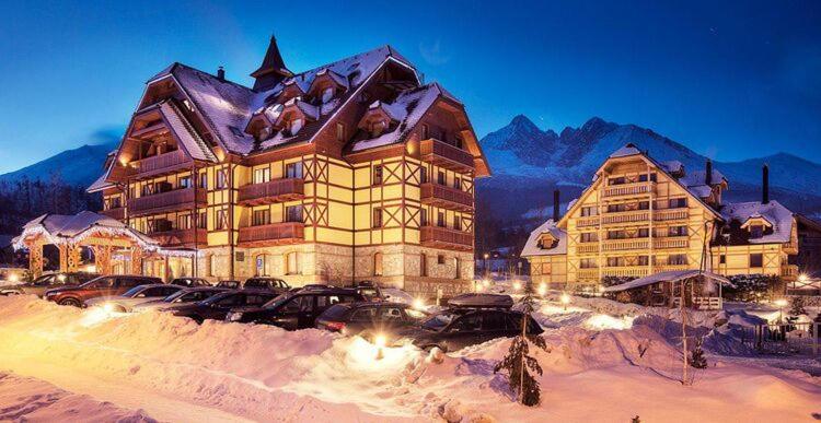 a large building with cars parked in the snow at Hotel Kukučka Apartment C104 Tatranská Lomnica in Vysoké Tatry