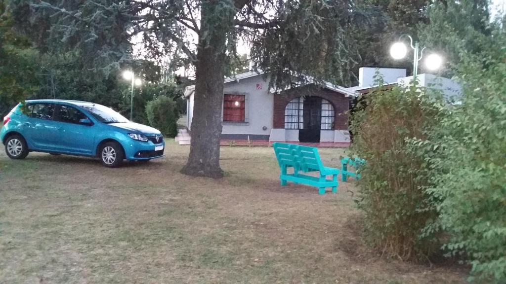 un coche azul estacionado junto a un árbol y un banco azul en El Hornero en Tandil