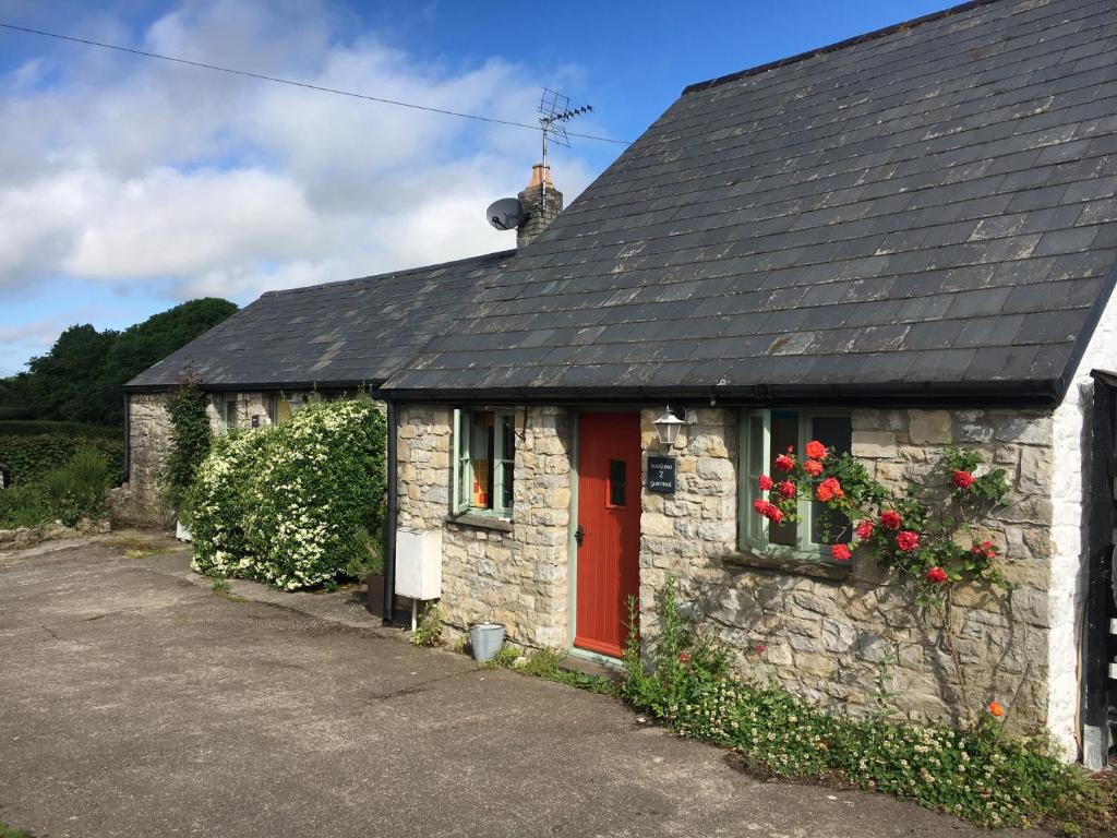 a stone cottage with a red door and flowers at Swallow Cottage in Cowbridge