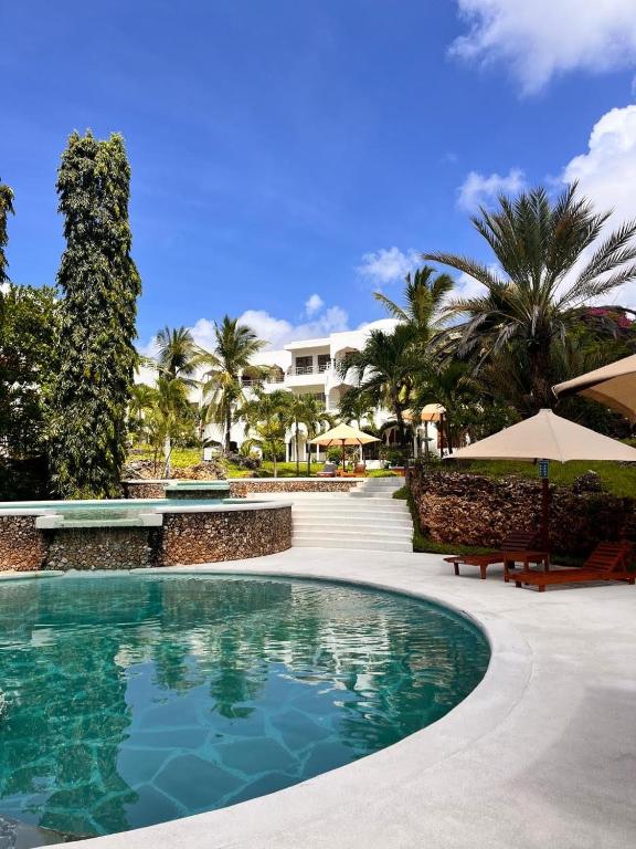 a pool at a resort with palm trees and umbrellas at Beverly Suites - Two Bedroom Apartment 2-5min to Beach in Malindi