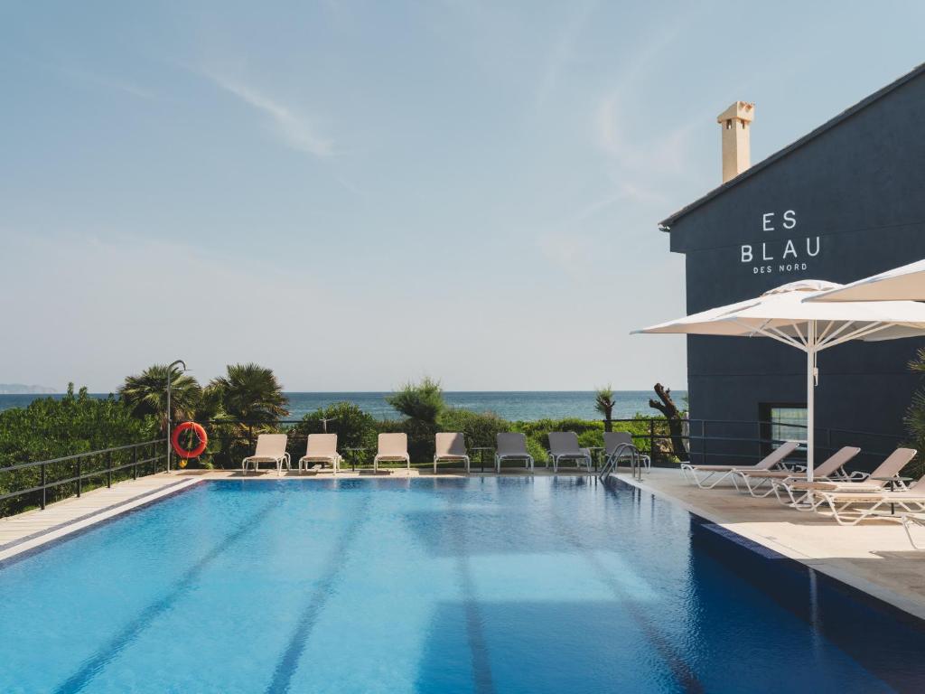 a swimming pool with chairs and umbrellas next to a building at Hotel Es Blau Des Nord in Colonia de Sant Pere