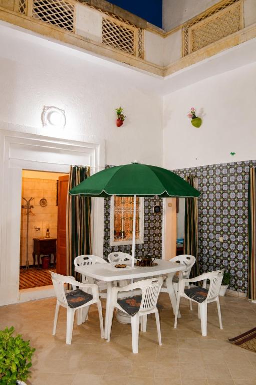a white table and chairs with a green umbrella at El Hamra Maison Traditionnelle in Mahdia