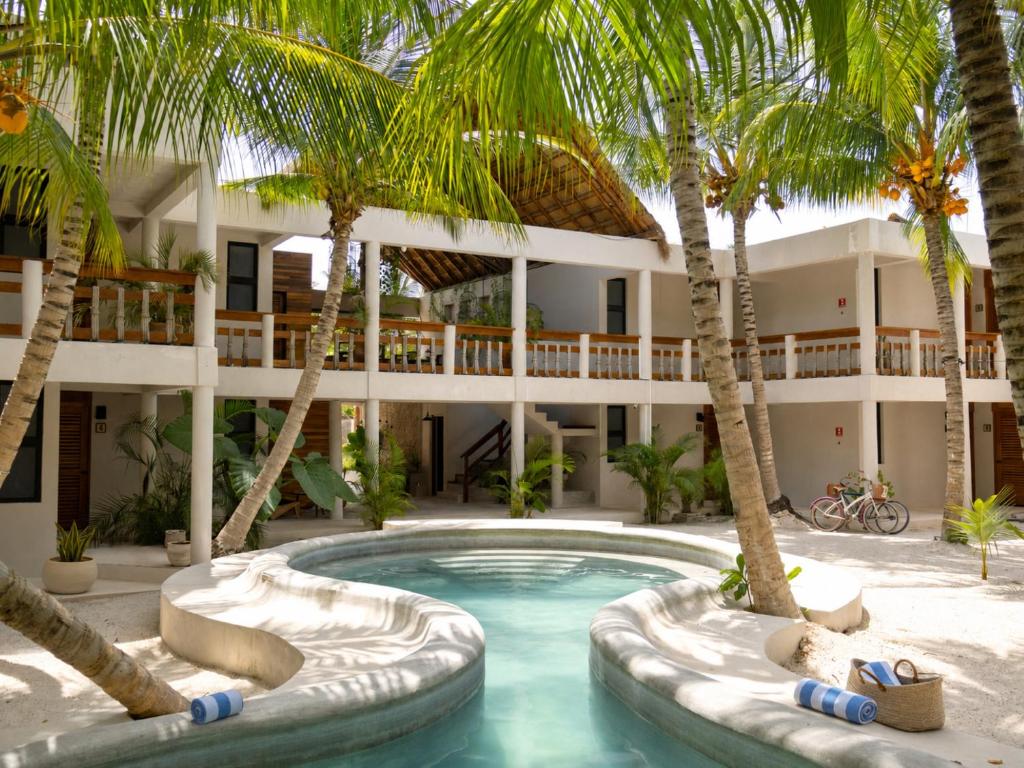 a pool in front of a hotel with palm trees at Casa del Viento by ÓOL Hotels in Holbox Island