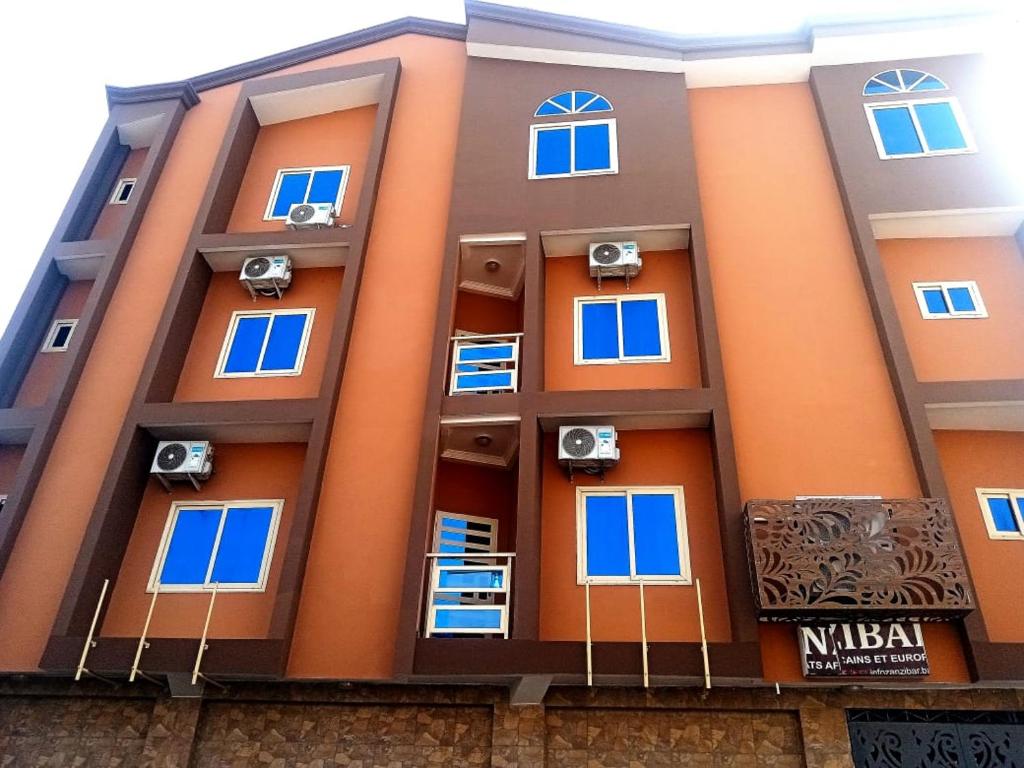 an orange building with blue windows and speakers at Hotel Mandelson in Godomey