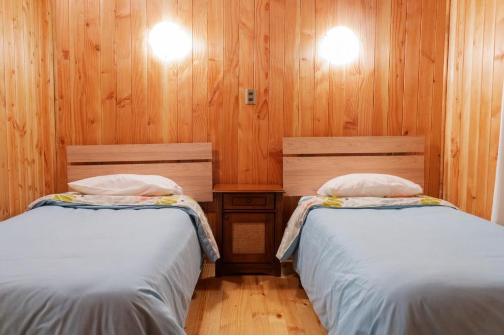 two beds in a room with wooden walls and wooden floors at Cabañas en neltume in Neltume