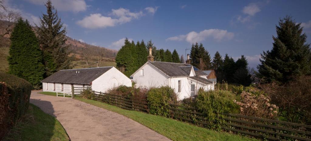 a white house on a hill next to a fence at Shegarton Farm Cottages in Luss