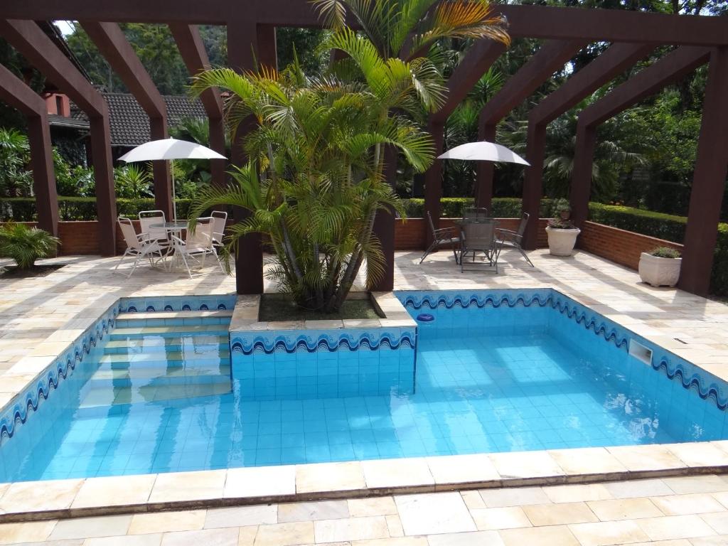 a blue swimming pool with a pergola and a palm tree at Pousada da Mantiqueira in Visconde De Maua