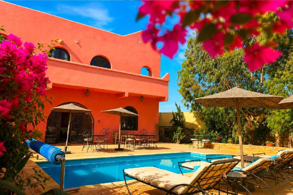 a swimming pool with chairs and umbrellas next to a building at Villa Nouran - Chambre D'Hôte in Ghazoua