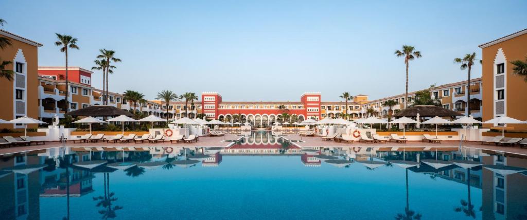 a large swimming pool in a resort with palm trees and buildings at Palacio de Sancti Petri, a Gran Meliá Hotel - The Leading Hotels of the World in Chiclana de la Frontera