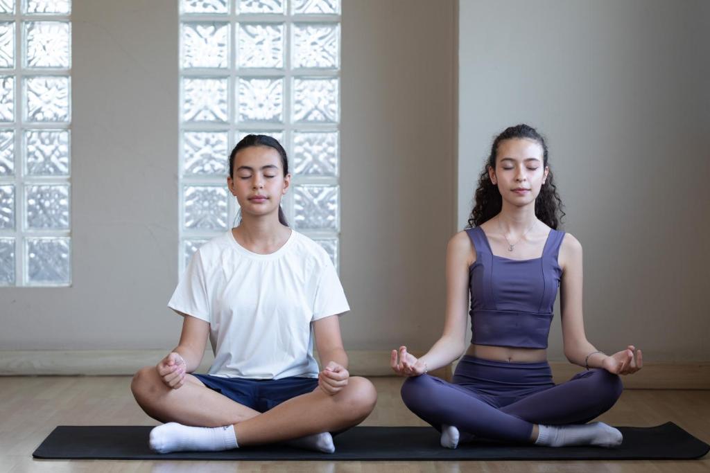 Two guests practising seated yoga on a mat in a bright studio.