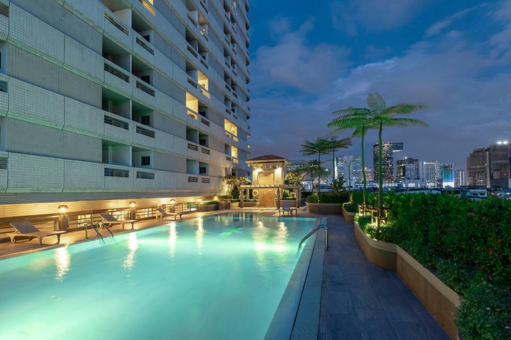 An illuminated rooftop pool overlooking a city skyline at dusk.