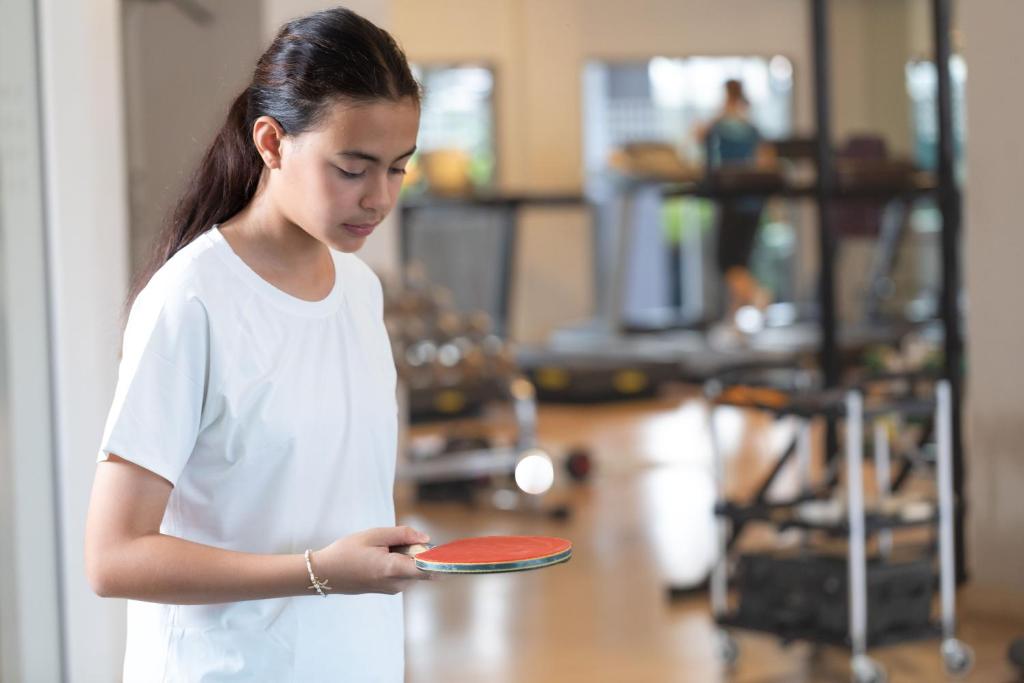 A staged fitness-room scene with a woman holding a table-tennis paddle beside exercise equipment.