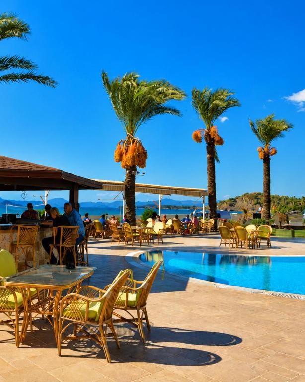 a pool with palm trees and a table and chairs at Sunset Beach Club Denize Sıfır Özel Plaj Apart in Fethiye