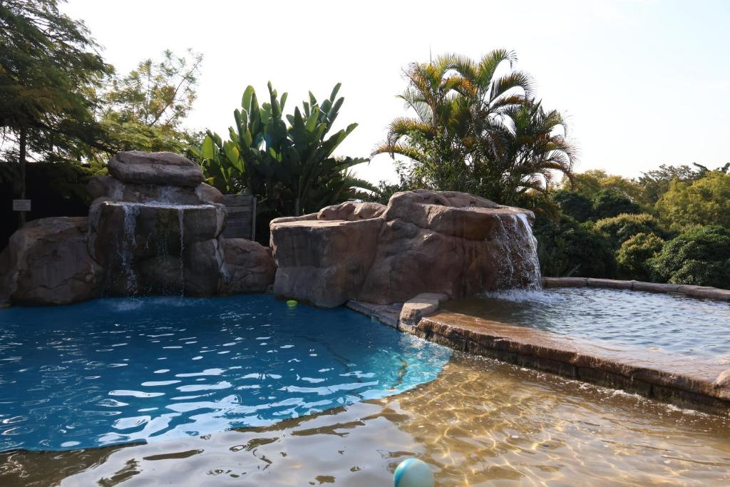 a pool with a waterfall and rocks in a backyard at Numbi Hills Self-Catering in Hazyview