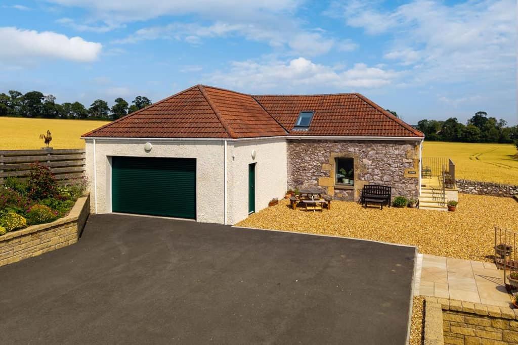 a house with a garage and a yellow field at Converted Barn - Romantic Countryside Escape in Cupar