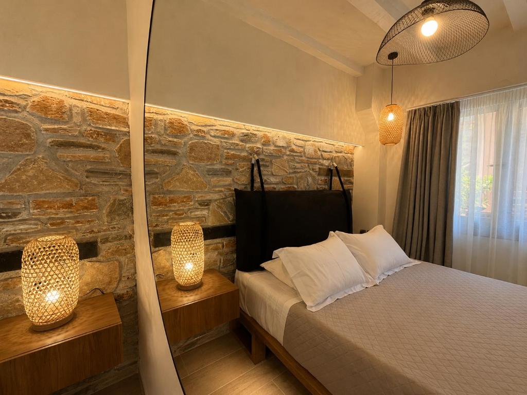 a bedroom with a stone wall and a bed with two lights at TERPOU StoneHouse & Suites in Volos