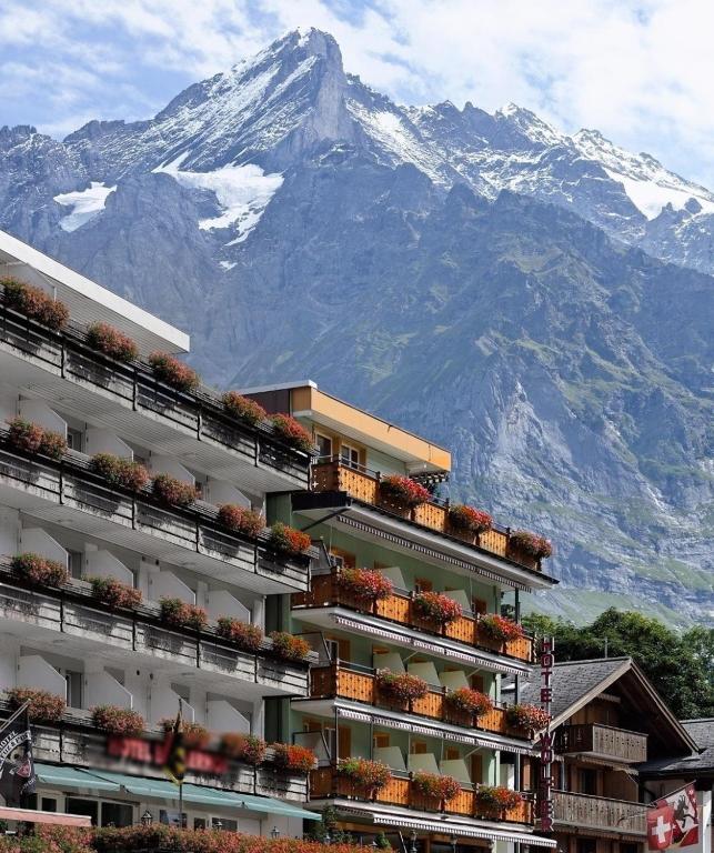 a building with plants on the balconies with a mountain at Hotel Central Wolter - Grindelwald in Grindelwald
