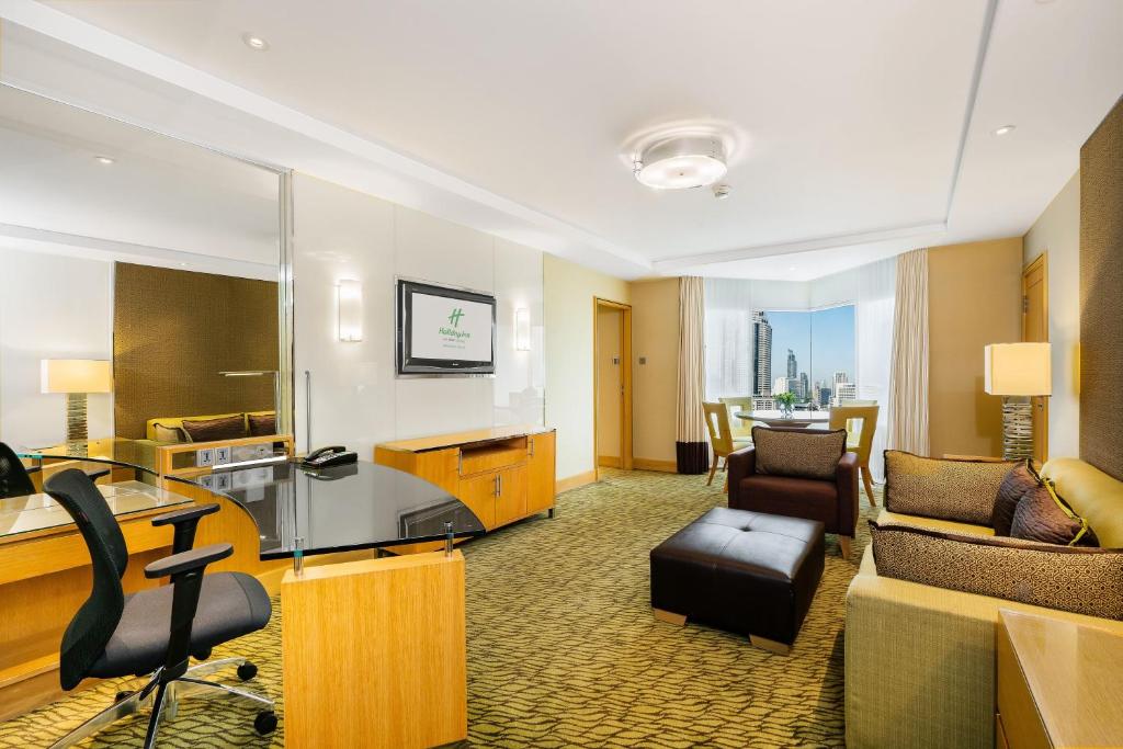 A spacious suite-style room combining a desk, lounge seating, television, and city view.