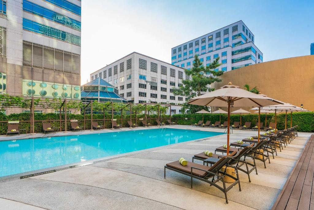 A large outdoor pool deck lined with loungers and shaded umbrellas among city buildings.