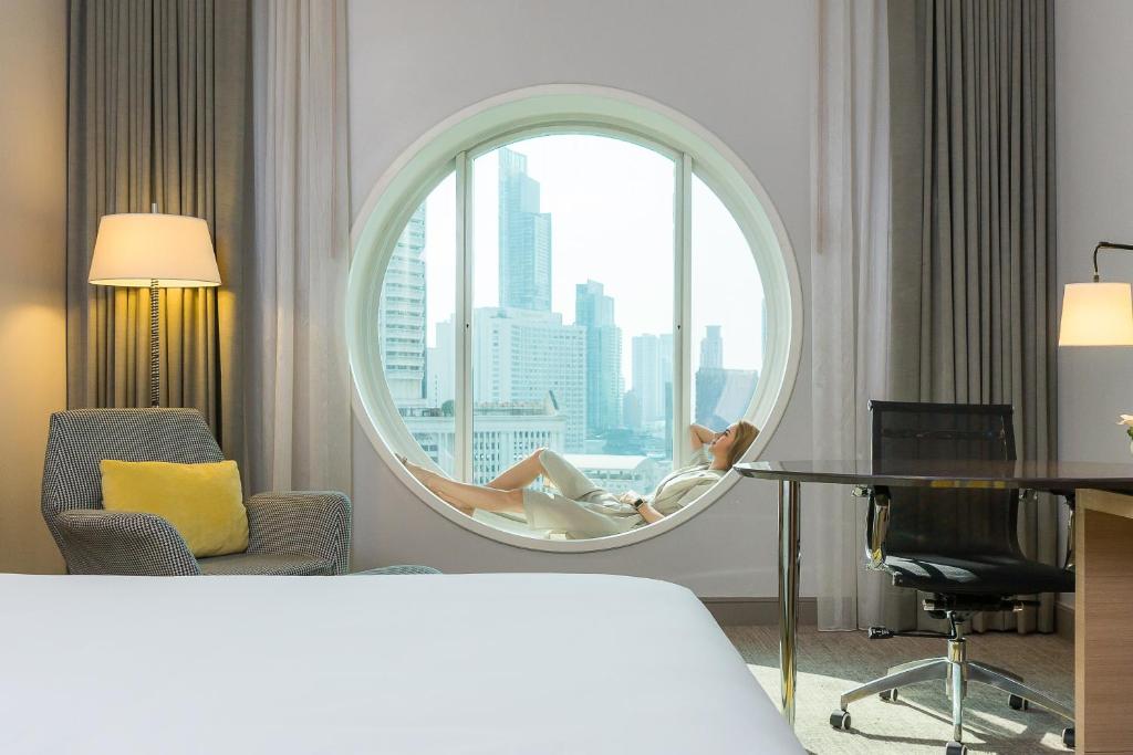 A guest room view centered on a round city-facing window and compact desk.