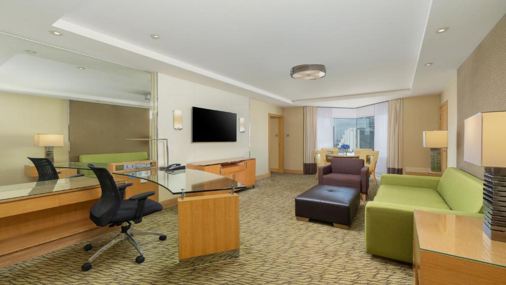 A hotel sitting room with two workstations, a television and multiple lounge seats.